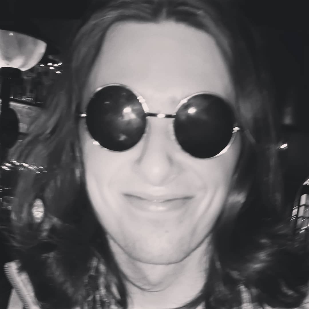 A black and white shot of Paul smiling, wearing Lennon shades